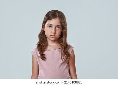 Front View Of Serious Little Girl Looking At Camera. Portrait Of Beautiful Caucasian Female Child Wearing Pink T-shirt. Childhood Concept. Isolated On White Background. Studio Shoot. Copy Space