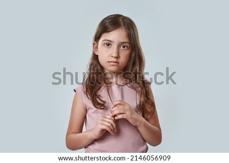 Front view of serious little girl touching her hair and looking at camera. Beautiful caucasian female child wearing pink t-shirt. Childhood concept. Isolated on white background in studio. Copy space