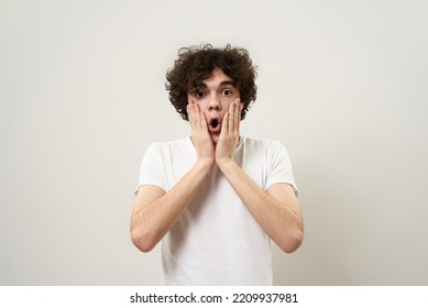 Front view of shocked caucasian teenage boy with open mouth looking at camera. Curly guy of zoomer generation. Concept of modern youngster lifestyle. Isolated on white background in studio. Copy space - Powered by Shutterstock