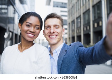 Front view shot of business people standing together outdoors, making selfie with mobile phone and smiling. Business man and woman  having fun outside the office during the break - Powered by Shutterstock