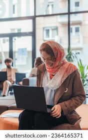 Front view shot of muslim businesswoman working on lap top and laughing while discussing with her colleague - Shutterstock ID 2364165371