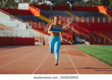 Front view shot of a woman athlete running on a race track in a sports arena. Athletic female training for a sport race competition or working out at the stadium. Sprinter or marathon racer. - Powered by Shutterstock