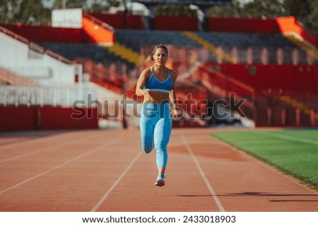 Front view shot of a woman athlete running on a race track in a sports arena. Athletic female training for a sport race competition or working out at the stadium. Sprinter or marathon racer.