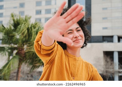 Front view of a shy latin girl hiding from the camera. Happy hispanic young woman smiling and covering her face with her hand palm. High quality photo