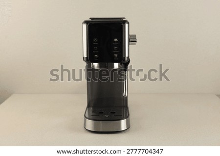 Front view of a simple, black coffee machine, isolated on a minimalist beige base, with bright light