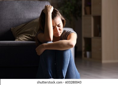 Front View Of A Single Sad Teen Sitting On The Floor In The Living Room At Home With A Dark Background