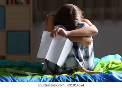 Front View Of A Single Sad Teen Lamenting Sitting On Her Bed After Reading A Letter With A Dark Light In The Background