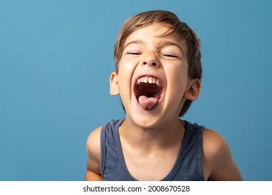 Front view of small caucasian boy four years old standing in front of blue background studio shot playful child making faces happiness and joy concept