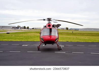 Front View of a Small Red Utility Helicopter Parked at an Airport on an Overcast Day