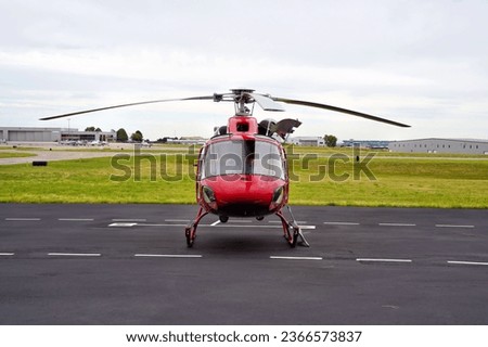 Front View of a Small Red Utility Helicopter Parked at an Airport on an Overcast Day