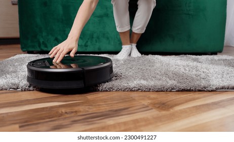 Front view of smart self-service automatic device cleaning the floor carpet while woman resting on the couch,4k
