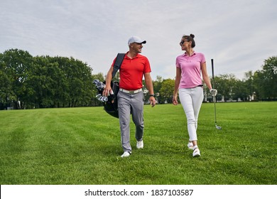 Front view of a smiling lady with a golf club walking next to a professional coach - Powered by Shutterstock