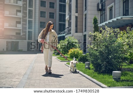 Front view of a smiling long-haired pretty woman taking her cute pet for a walk