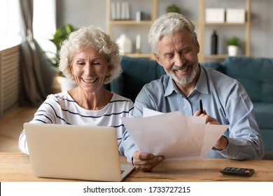 Front View Smiling Old Woman Entering Payment Data Into Banking Application On Computer While Pleasant Mature Husband Reading Paper Tax Document. Happy Senior Married Couple Managing Family Budget.