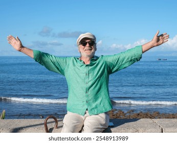 Front view of smiling senior retired man sitting near the beach with outstretched arms enjoying freedom and a sunny day. Authentic retirement lifestyle