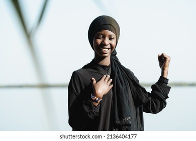 Front view of a smiling young African girl with one hand on her chest and raised fist, symbolizing the power, confidence and self-esteem of the women of her continent's future generations
