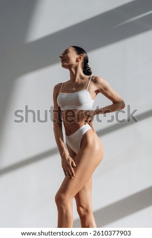 Front view, standing and posing. Beautiful young woman with slim body type is indoors.