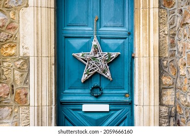 Front view of a star-shape Christmas decoration made of branches and pine cones, hanging on the blue front door with moldings of an old townhouse. - Powered by Shutterstock