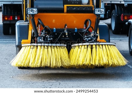 Front view of a street sweeper with two large yellow brushes, parked on an asphalt surface