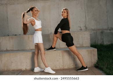 Front view, stretching exercises. Two sportive women are outdoors together.