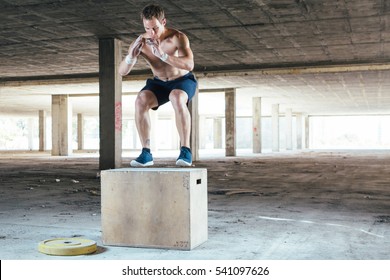 Front view of strong man doing box jumps in abandoned building. 