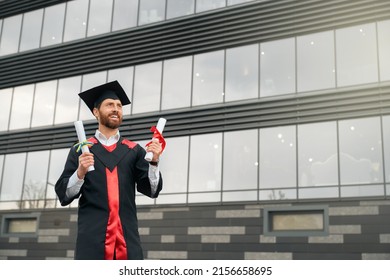 Front view of student with beard graduating from college, getting degree. Male wearing graduate gown and cap, standing, holding diploma, smiling, happy. Concept of education. - Shutterstock ID 2156658695