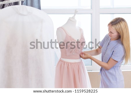 Front view of successful wedding dressmaker owner measuring materials on mannequin in office or workshop. Talented female seamstress working with textile for sewing clothes