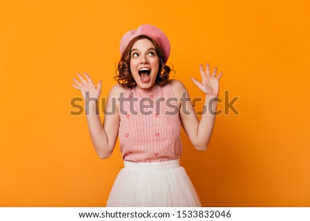 Front view of surprised french girl with tattoos. Studio shot of amazed elegant woman in beret isolated on yellow background.