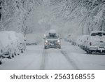 Front View of SUV Car driving through urban City during heavy Snowfall.  Street, Cars and Trees covered in heavy Snow; Copyspace