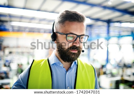 Front view of technician or engineer with headset standing in industrial factory.