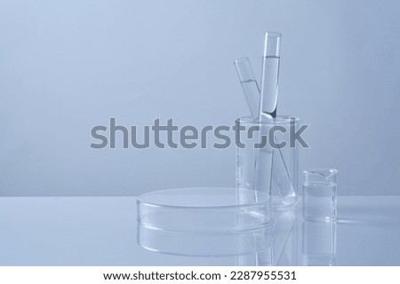 Front view of test tubes filled colorless liquid in beaker and petri dish upside down form an empty platform to display cosmetic product. Science laboratory research and development concept