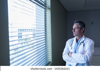 Front View Of Thoughtful Caucasian Mature Male Doctor Looking Through Window In The Hospital