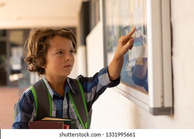 Front view of a thoughtful Caucasian schoolboy pointing at noticeboard in the corridor at schoiol - Powered by Shutterstock