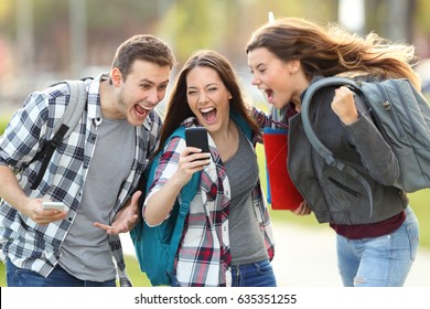 Front view of three excited students receiving good news on line in a mobile phone in an university campus or street - Powered by Shutterstock