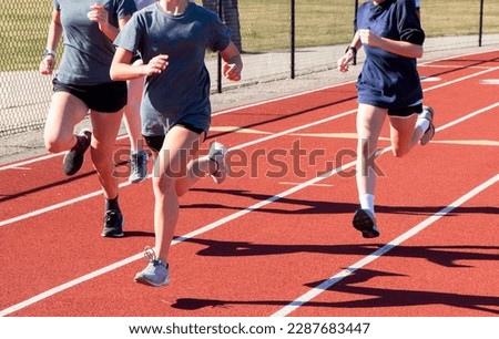Front view of three high school girls running fast in lanes on a red track during practice.