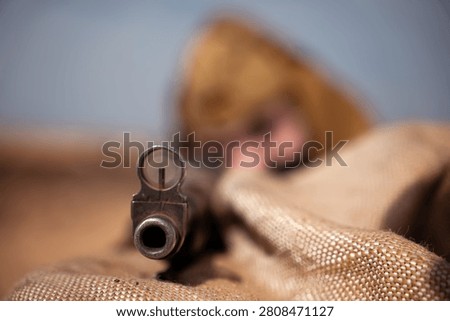 Front view through the sights of rifle held by a Soviet sniper during a World War II military reenactment. Concept of Eastern Front combat, battlefield tension, and historical reconstruction.