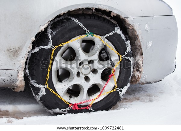 Front view of tire chains on car wheel on dirty\
vehicle in snow
