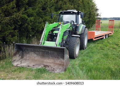 Front View Of Tractor With Front End Loader And Trailer For Excavator On Rear. Copy Space.