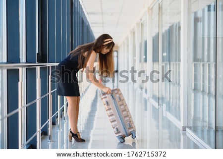 Front view of a traveler woman walking carrying a suitcase in an airport corridor