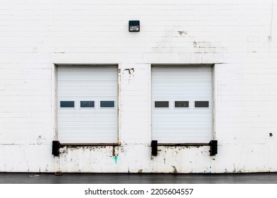 Front View Of A Truck Loading Bay With Rubber Bumpers In The White Concrete Wall Of A Warehouse With A Closed White Roller Shutter Door