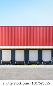 Front view of a truck loading dock at a warehouse in the suburbs of Paris, France, with four white roller shutter doors closed under a red corrugated metal siding.