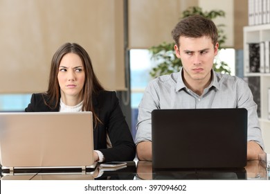 Front view of two angry businesspeople using computers disputing at workplace and looking sideways each other with envy - Powered by Shutterstock