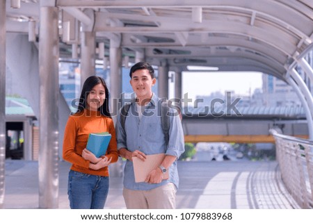 Front view of two asian students walking and talking in an university campus.