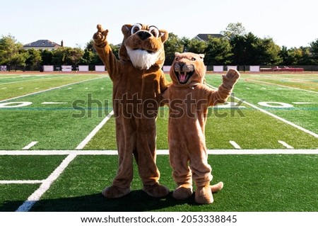 Front view of two cougar mascots waving to the camera standing on a green turf football field.