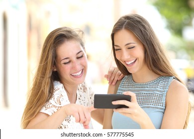 Front View Of Two Friends Watching Media Content In A Smart Phone Outdoor In The Street