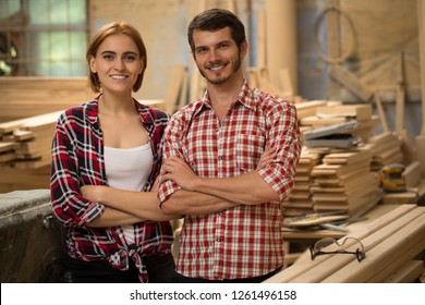 Front view of two handsome and positive carpenters standing, looking at camera and posing. Young and talented woodworkers smiling, wearing in checked shirts. Background of joiner's shop. - Powered by Shutterstock