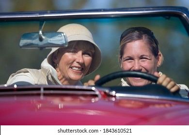 Front View Of Two Joyous Women Driving In An Red Convertible On A Sunny Day.