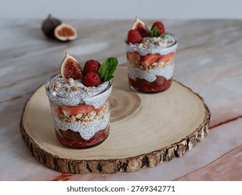 Front view of two layered chia desserts with berries and granola on natural wood slice