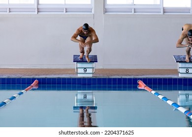 Front view of two male swimmers at swimming pool, jumping from starting blocks, plunging into water. Swimmers training hard for competition. - Powered by Shutterstock