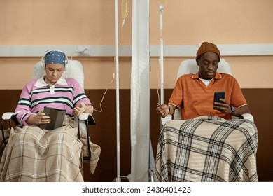 Front view at two people sitting in chairs with IV drip tubes and getting chemotherapy treatment in clinic - Powered by Shutterstock